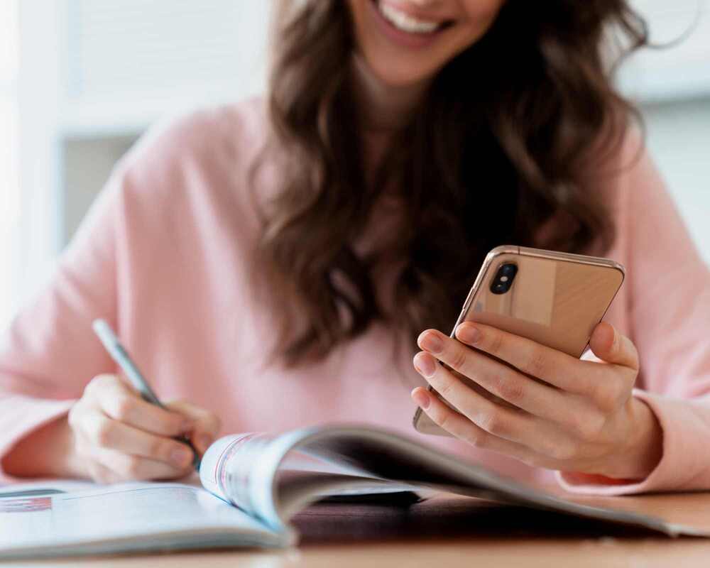 Woman smiling whilst looking at her phone and writing notes