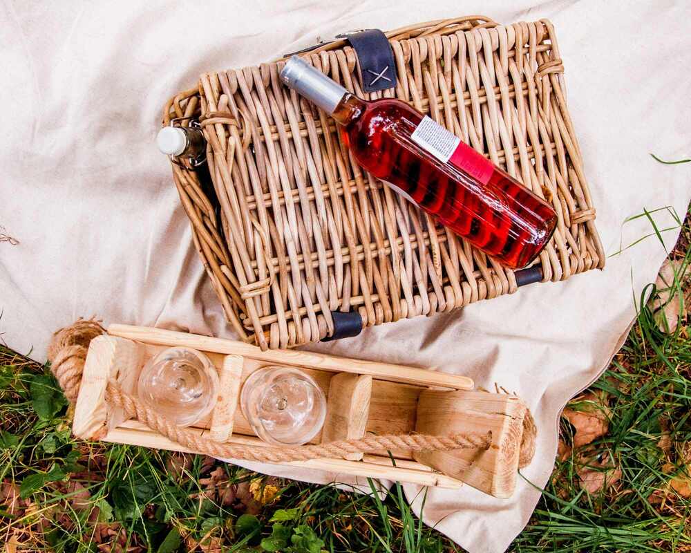 A picnic basket, bottle of wine and wine glasses placed on a picnic blanket
