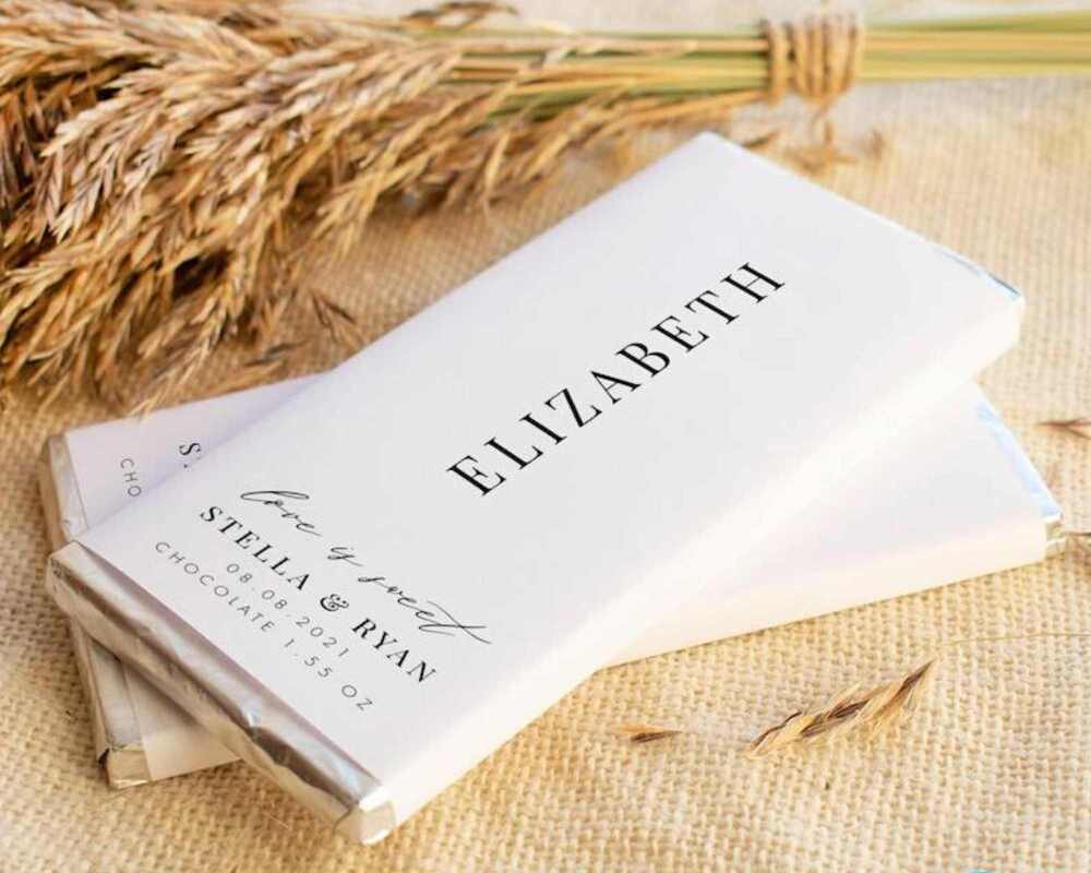 Custom chocolate bar wrappers. There are two chocolate featuring these wrappers. The chocolates are placed on a table and there is dried grass next to them.