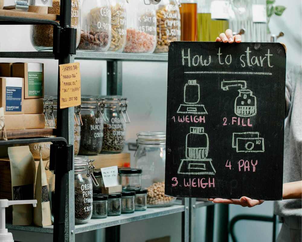 Shop with foods displayed in large jars and cardboard boxes. There is a sign that says: 'How to start  - weigh, fill, weigh, pay'