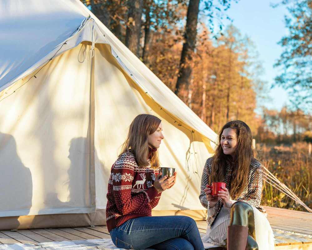 Two women drinking coffee on the deck of a glamping tent