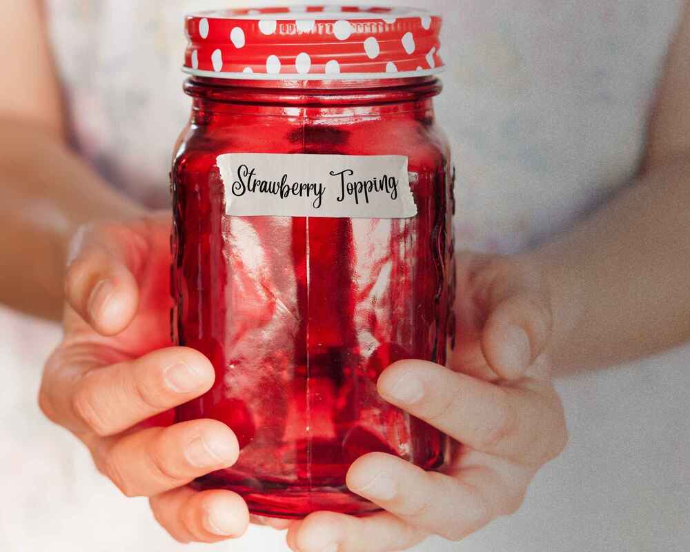 Hands holding a jar filled with strawberry topping