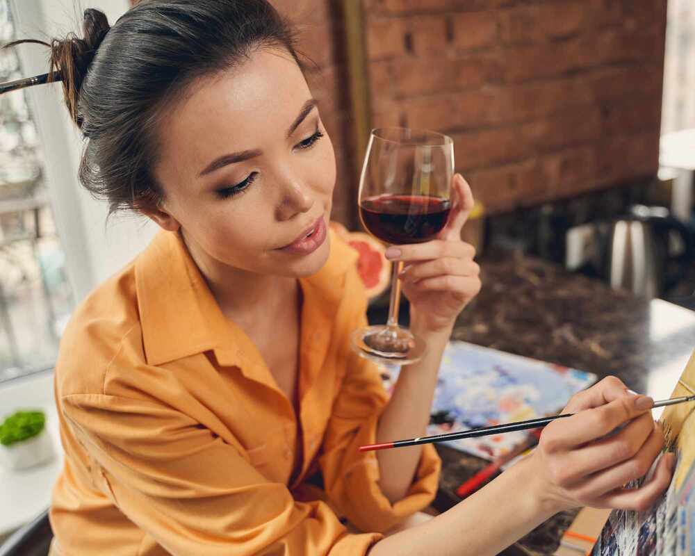 A woman painting whilst holding a glass of wine