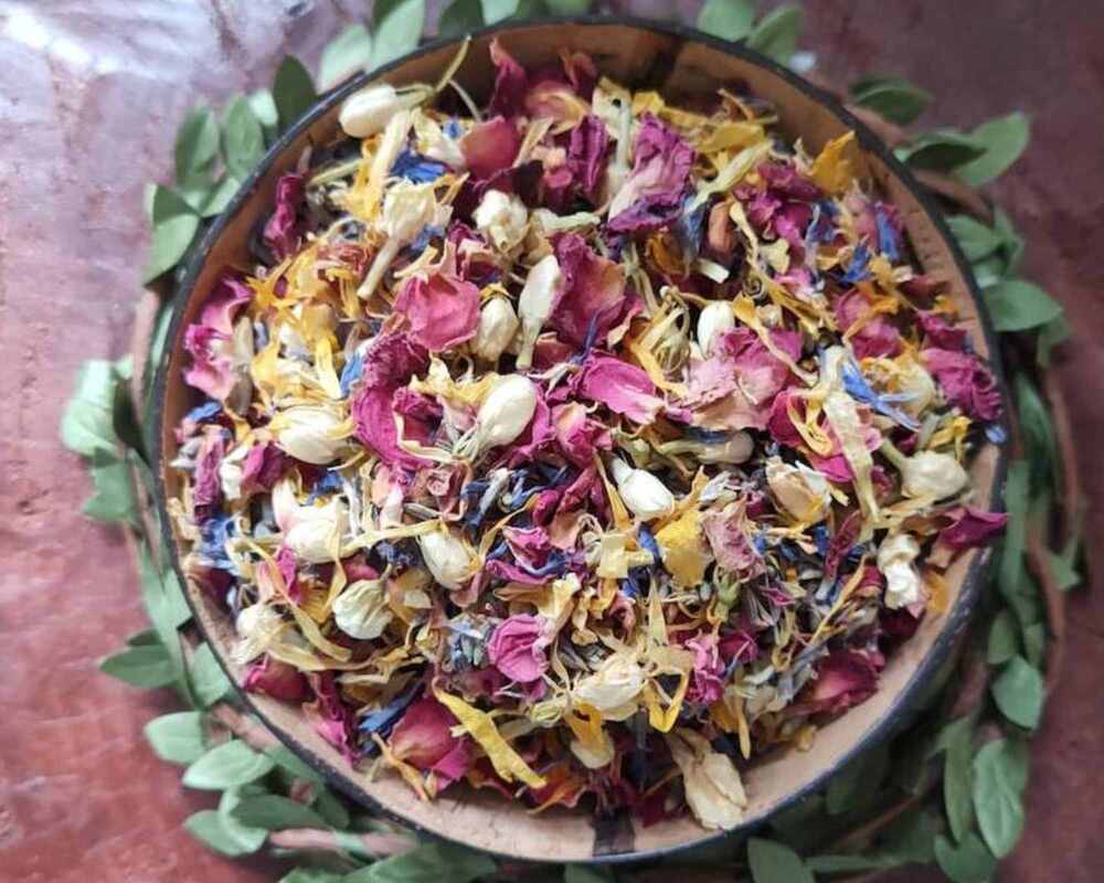 Dried flower confetti in a small bowl. The bowl in surrounded by leaves and is on a table