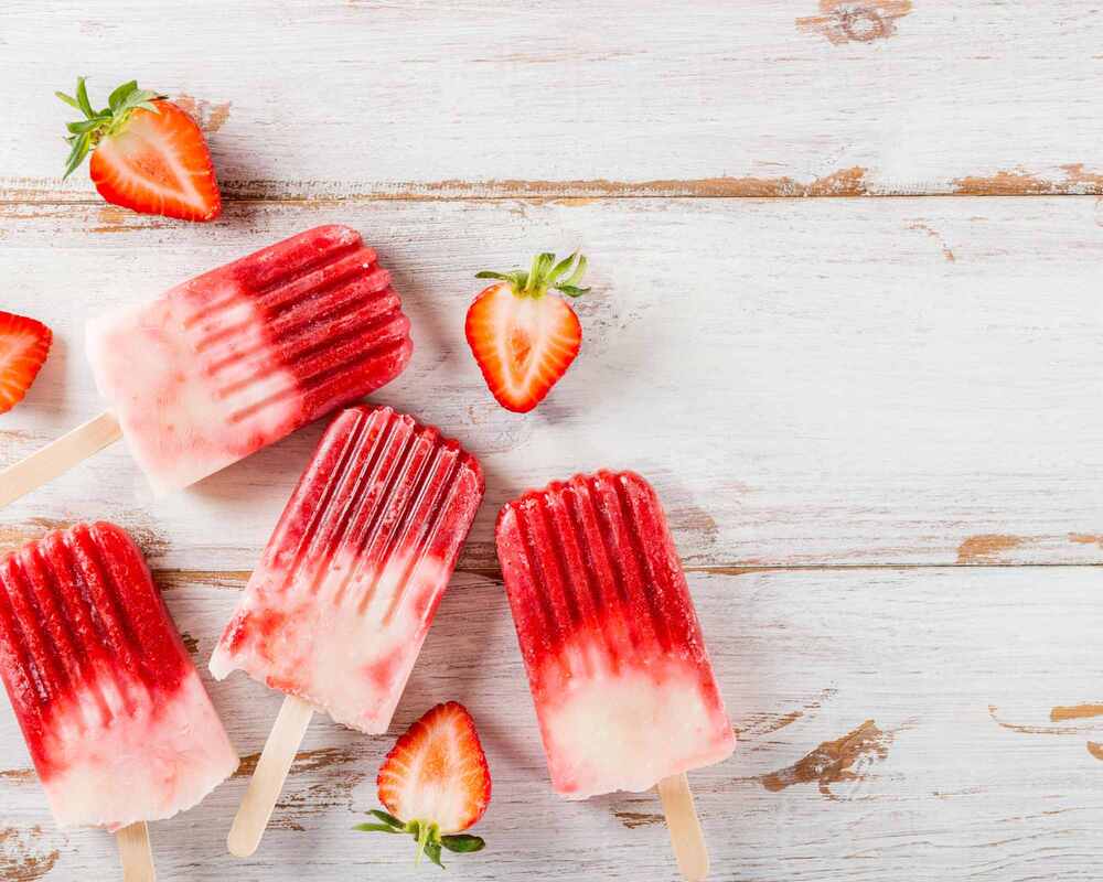Strawberry popsicles on a white table. They are surrounded by strawberries